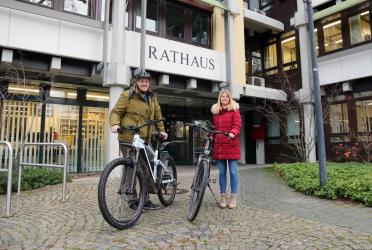 Ein Mann und eine Frau stehen mit ihren Fahrrädern vor dem Rathaus.