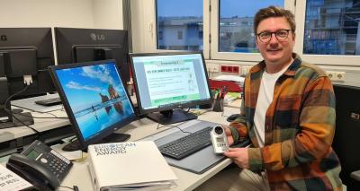 Ein Mann sitzt vor einem Computer. In der Hand hält er ein Strommessgerät.