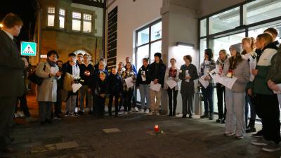 Menschen stehen mit Kerzen in der Hand auf der Straße um einen Stolperstein